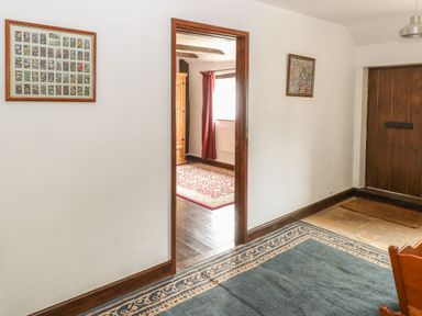 A hallway with a blue patterned rug a wooden door and framed pictures on the walls at The Old Barn in Walcott
