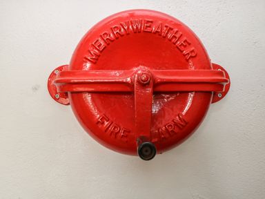 A red merryweather fire alarm mounted on a white wall at The Old Barn in Walcott