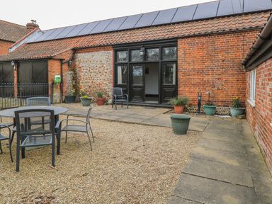 An outdoor patio area with metal table and chairs and potted plants outside a brick building at The Old Barn in Walcott
