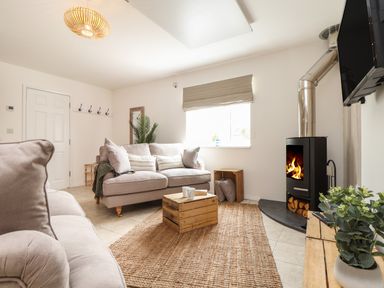 A living room with two sofas a wooden crate table a fireplace and a TV at The Old Post Office in Porthleven