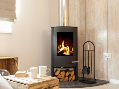 A room with a wood burning stove with firewood underneath and fireplace tools next to it at The Old Post Office in Porthleven