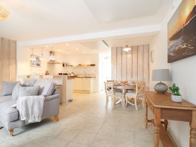 An open plan living room with a grey sofa and a kitchen with a countertop in the background at The Old Post Office in Porthleven