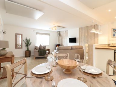 A dining table set with plates and glasses in an open living and kitchen area at The Old Post Office in Porthleven