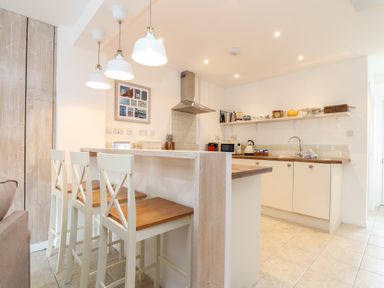 A kitchen with a breakfast bar and three chairs white cabinets and open shelves at The Old Post Office in Porthleven