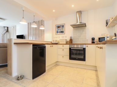 A kitchen with white cabinets oven microwave and pendant lights at The Old Post Office in Porthleven