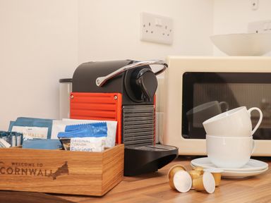 A kitchen counter with a coffee machine cups and capsules next to a microwave at The Old Post Office in Porthleven
