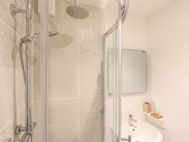 A bathroom with a shower area a sink a mirror and a small shelf at The Old Post Office in Porthleven