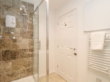 A bathroom with a glass shower enclosure a white door and a towel on a radiator at The Old Post Office in Porthleven