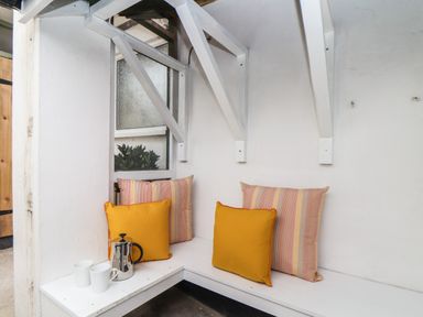 A white corner bench with yellow and striped cushions and a coffee pot with two white mugs at The Old Post Office in Porthleven