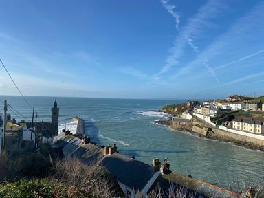 A coastal village with rooftops a clock tower a pier and ocean at The Old Post Office in Porthleven