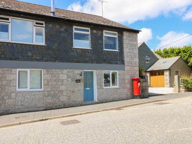 A stone house with blue door and red postbox on the street at The Old Post Office in Porthleven