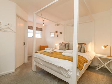 A bedroom with a four-poster bed pillows bedside tables lamps and a chair at The Old Post Office in Porthleven