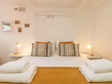 A bedroom with a double bed two bedside tables with lamps and folded towels at The Old Post Office in Porthleven