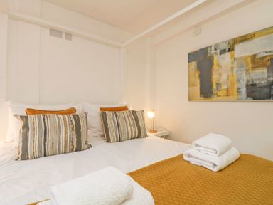 A bed with striped and solid pillows folded towels on a brown blanket and abstract painting on the wall at The Old Post Office in Porthleven