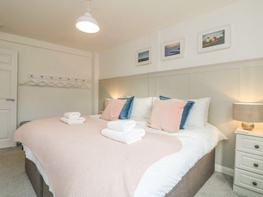 A bedroom with a double bed with folded towels on the blanket and framed pictures on the wall at The Old Post Office in Porthleven