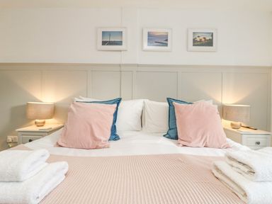 A bedroom with a double bed with pink and blue pillows bedside tables with lamps and folded white towels at The Old Post Office in Porthleven