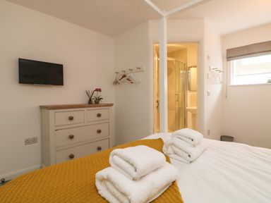 A bedroom with a bed with towels on a yellow blanket a dresser a wall-mounted television and an en suite bathroom at The Old Post Office in Porthleven