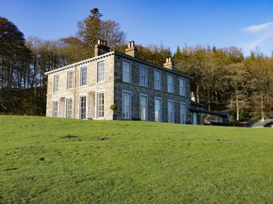 A stone house with multiple windows on a grassy hill with trees in the background at Silverholme Graythwaite near Hawkshead