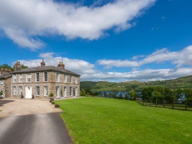 A stone house next to a driveway with green lawn and trees near a lake at Silverholme in Graythwaite near Hawkshead