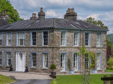 A stone house with blue-trimmed windows and white door surrounded by green lawn at Silverholme Graythwaite near Hawkshead