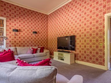 A living room with patterned red wallpaper a television on a stand and beige sofas with red cushions at Silverholme Graythwaite near Hawkshead