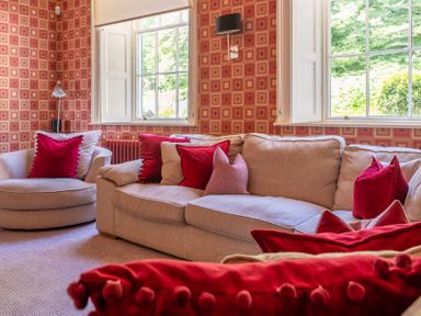 A sitting room with beige sofas and red cushions near windows with patterned wallpaper at Silverholme Graythwaite near Hawkshead