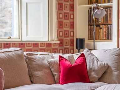 A beige sofa with a red pillow near a window and a floor lamp with books in the background at Silverholme in Graythwaite near Hawkshead