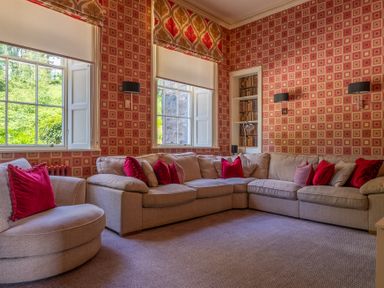 A sitting room with a beige sectional sofa and red cushions next to windows with white blinds at Silverholme in Graythwaite near Hawkshead
