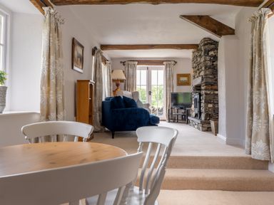 A living room with a blue sofa, stone fireplace, television, wooden dining table, and white chairs at Silverholme in Graythwaite near Hawkshead