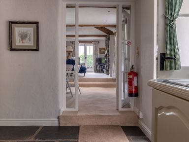 View through an open doorway showing a living room with chairs a lamp a television and a stone fireplace at Silverholme in Graythwaite near Hawkshead
