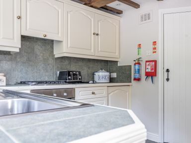 A kitchen with white cabinets a toaster a bread container a sink and safety equipment on the wall at Silverholme Graythwaite near Hawkshead