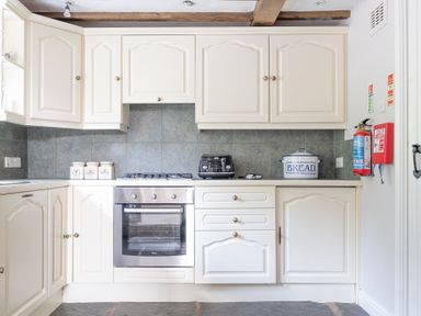 A kitchen with white cabinets a stainless steel oven a black toaster and a bread container at Silverholme in Graythwaite near Hawkshead