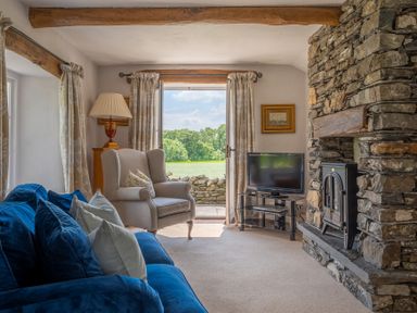 A living room with a blue sofa an armchair a television and a stone fireplace at Silverholme in Graythwaite near Hawkshead