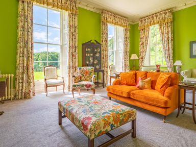 A sitting room with orange sofa floral armchairs and curtains with large windows at Silverholme in Graythwaite near Hawkshead