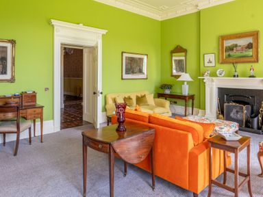 A living room with orange and yellow sofas a wooden desk a fireplace and framed pictures on green walls at Silverholme Graythwaite near Hawkshead