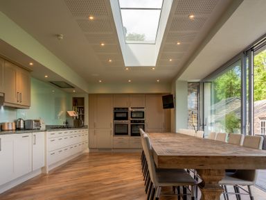 A kitchen with a long wooden dining table and beige chairs under a skylight at Silverholme in Graythwaite near Hawkshead