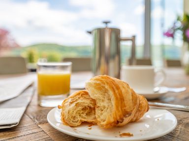 A croissant on a plate with a glass of orange juice a coffee pot and a cup on a wooden table at Silverholme in Graythwaite near Hawkshead