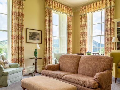 A living room with patterned curtains and a sofa facing a window at Silverholme in Graythwaite near Hawkshead