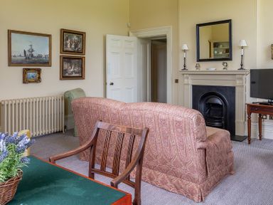 A living room with patterned sofa paintings on wall fireplace and wooden chair at Silverholme in Graythwaite near Hawkshead