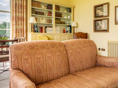 A sitting room with a patterned sofa a built in bookshelf with books and decor and framed pictures on the wall at Silverholme in Graythwaite near Hawkshead