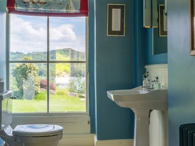 A bathroom with a toilet and sink and a window showing a garden and hills at Silverholme in Graythwaite near Hawkshead
