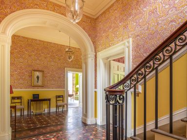 A hallway with patterned wallpaper wooden chairs table and an iron staircase railing at Silverholme Graythwaite near Hawkshead