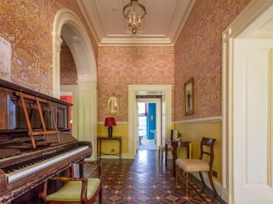 A hallway with patterned wallpaper a wooden piano and chairs at Silverholme Graythwaite near Hawkshead