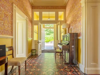 A hallway with patterned tile floor a piano a bench and yellow and patterned walls at Silverholme Graythwaite near Hawkshead