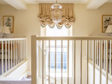 A staircase landing with white railings and beige curtains on a window at Silverholme Graythwaite near Hawkshead
