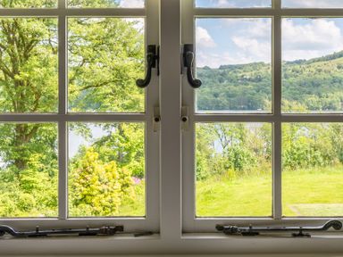 A window with decorative black handles overlooking green trees grass and distant hills at Silverholme in Graythwaite near Hawkshead
