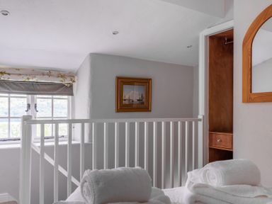 A stairway landing with a window a wooden framed painting a wooden mirror and rolled white towels on a bed at Silverholme in Graythwaite near Hawkshead