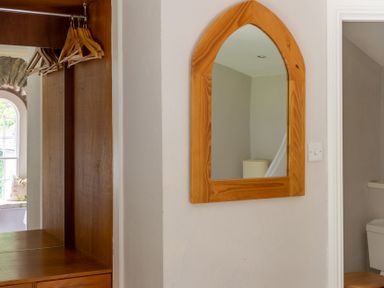 A wooden-framed mirror on a white wall next to a wooden wardrobe with hangers and a window seat in a room at Silverholme Graythwaite near Hawkshead