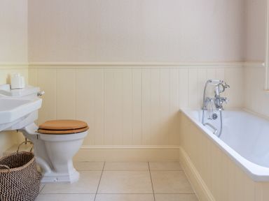 A bathroom with a toilet with wooden seat a bathtub with chrome faucet and a basket on tiled floor at Silverholme in Graythwaite near Hawkshead