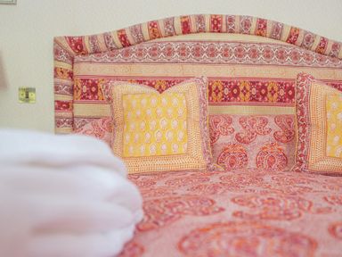 A bed with patterned red and yellow bedspread and cushions and a folded white towel at Silverholme in Graythwaite near Hawkshead